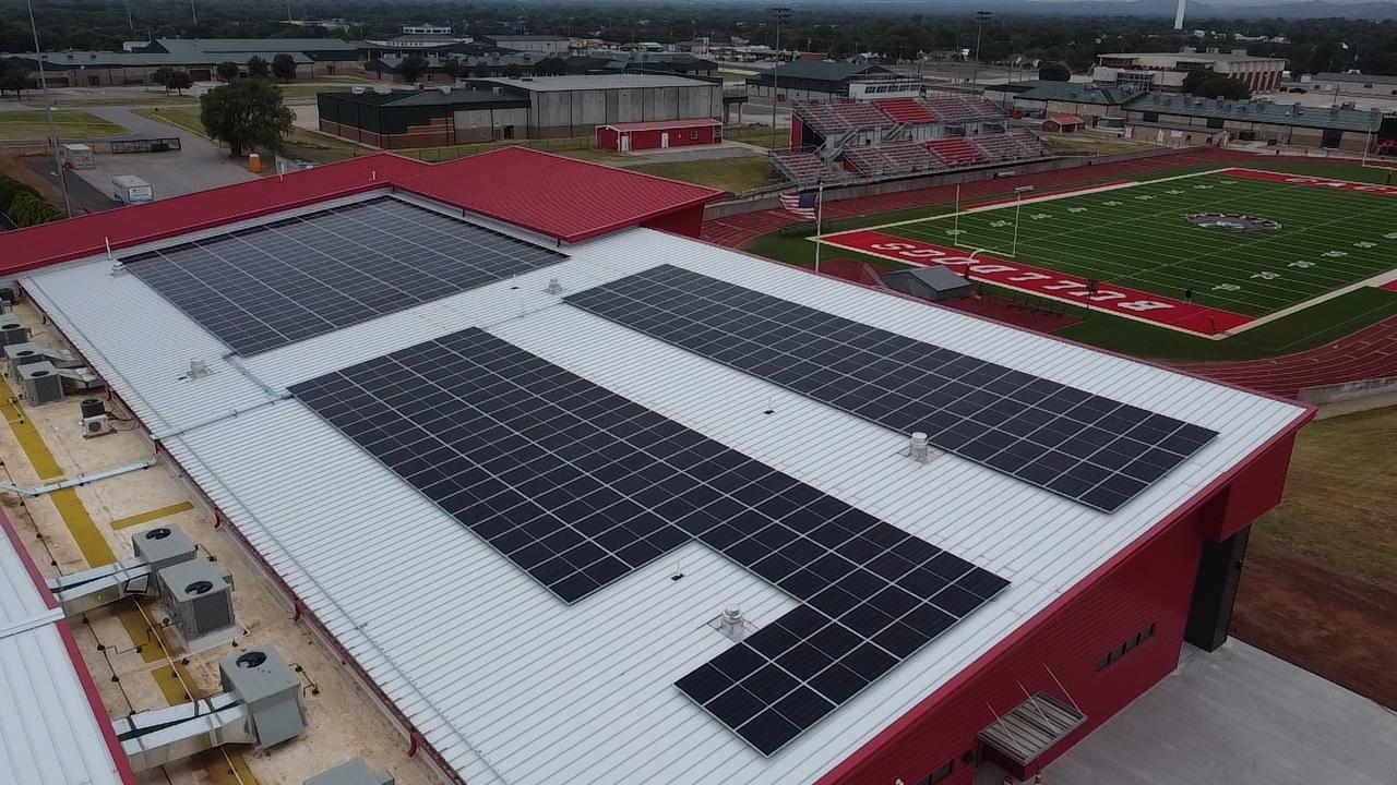 Aerial view of a rooftop solar array on an Oklahoma school building beside its football field